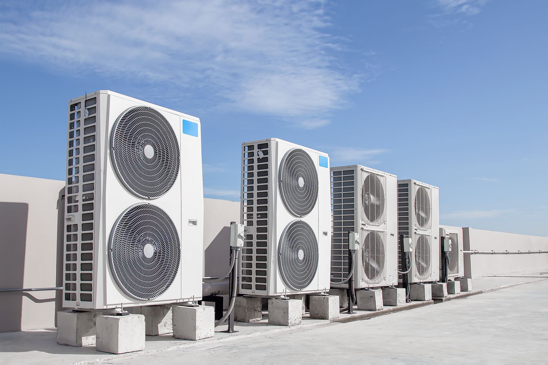 Air conditioning units lined up on a rooftop against a blue sky.