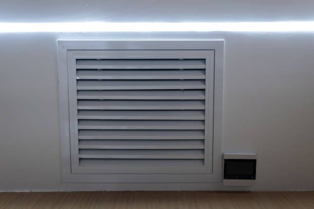 White wall-mounted air conditioning unit near a window, angled shot.