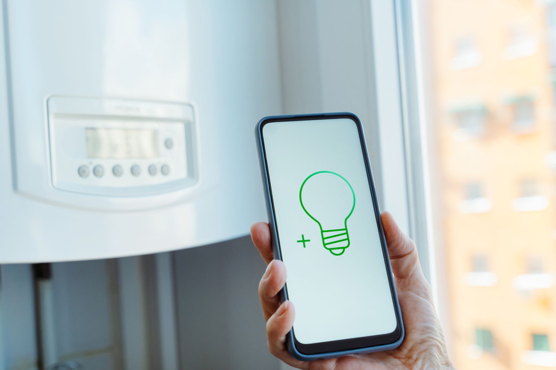 Hand holding phone with a green lightbulb icon in front of a white appliance.