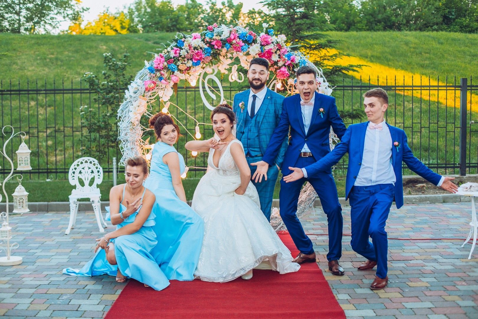 A bride and groom are posing for a picture with their wedding party on a red carpet.