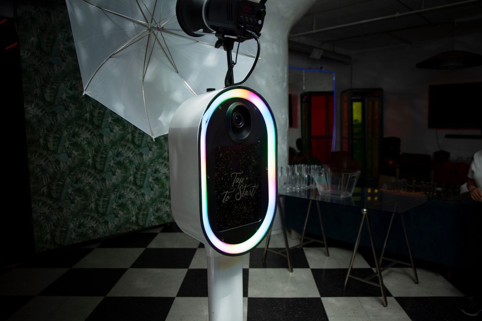 A photo booth with a camera and umbrella in a room with a checkered floor.