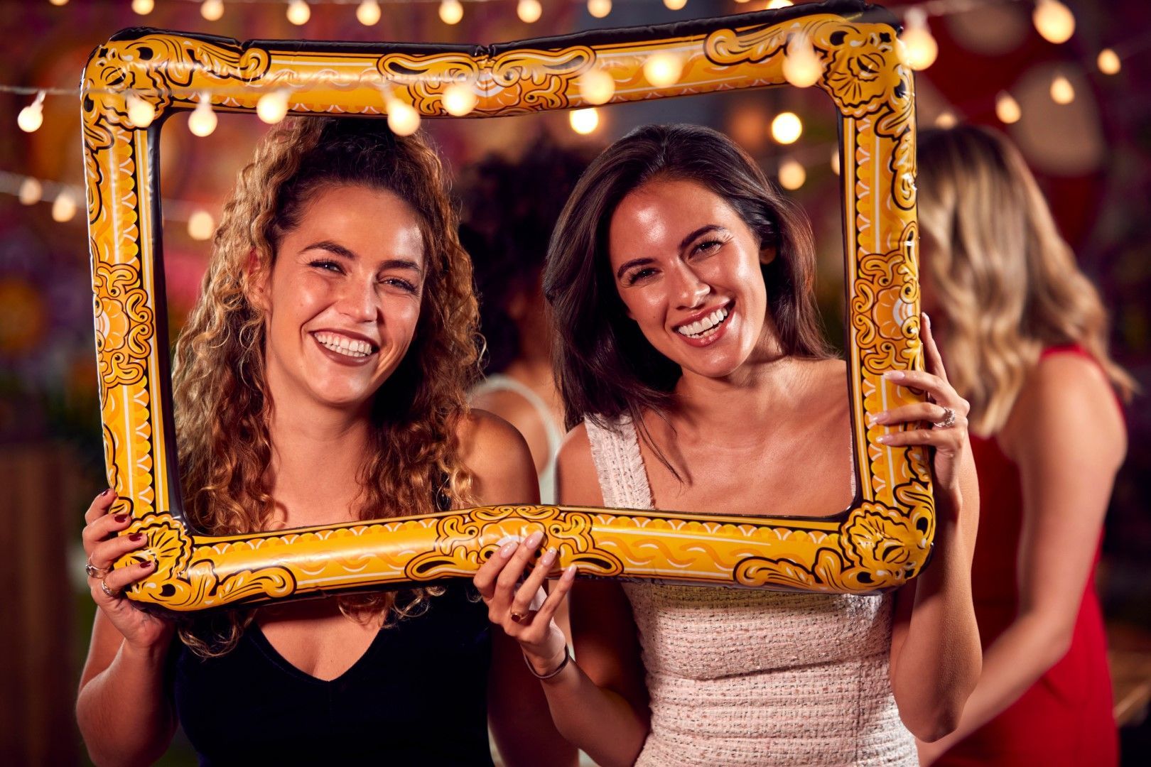 Two women are holding an inflatable picture frame at a party.