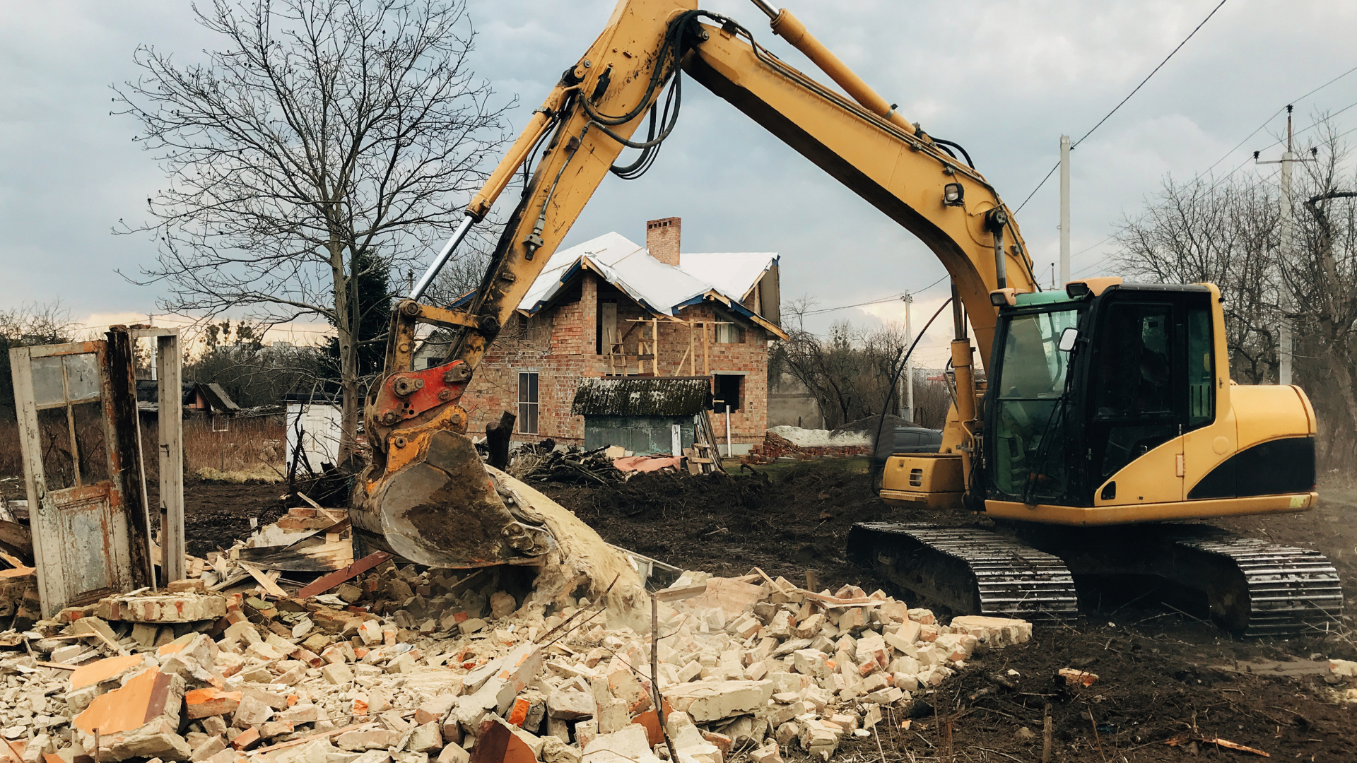 A yellow excavator is demolishing a brick house.