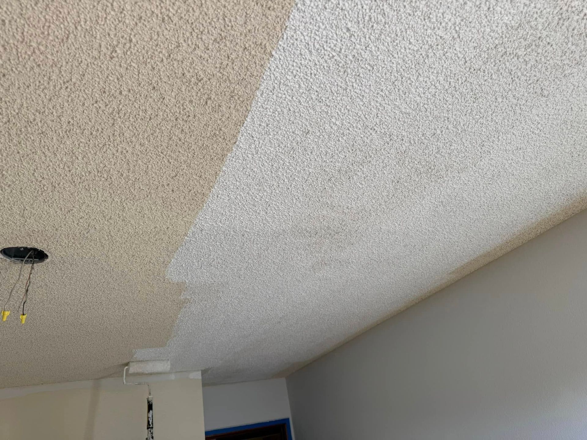A ceiling is being painted in a room with a roller.