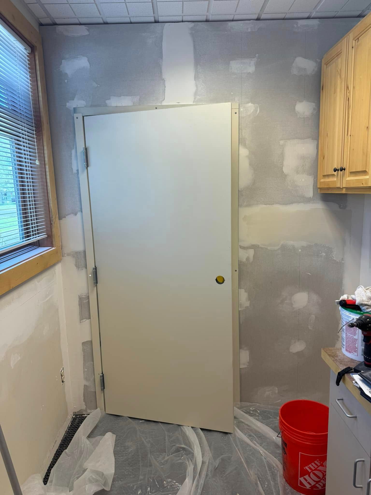 A room with a white door and a red bucket on the floor.
