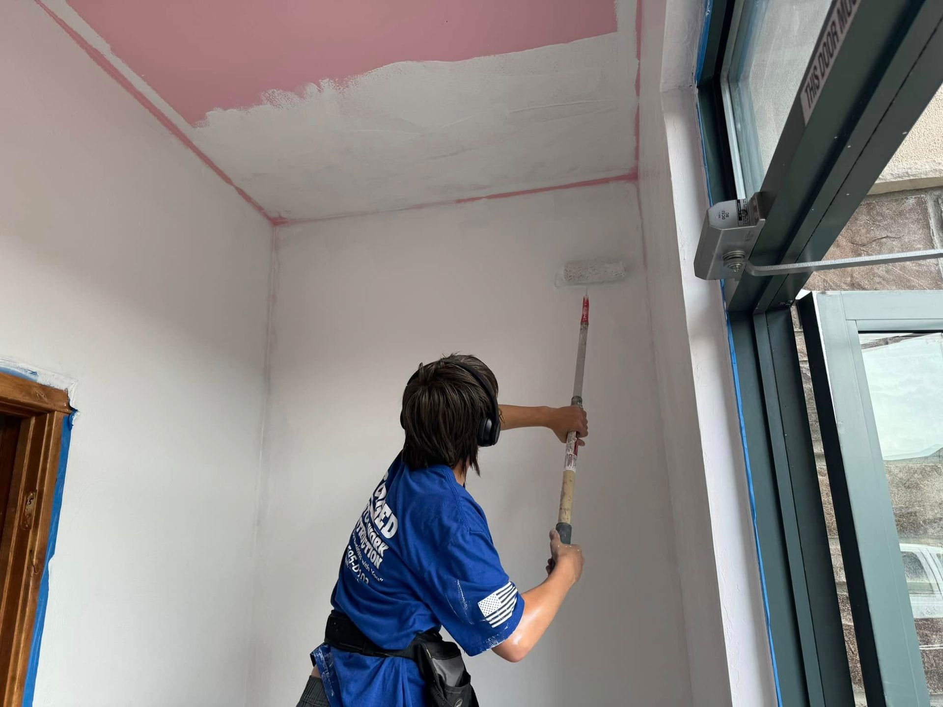 A man in a blue shirt is painting a wall with a roller.