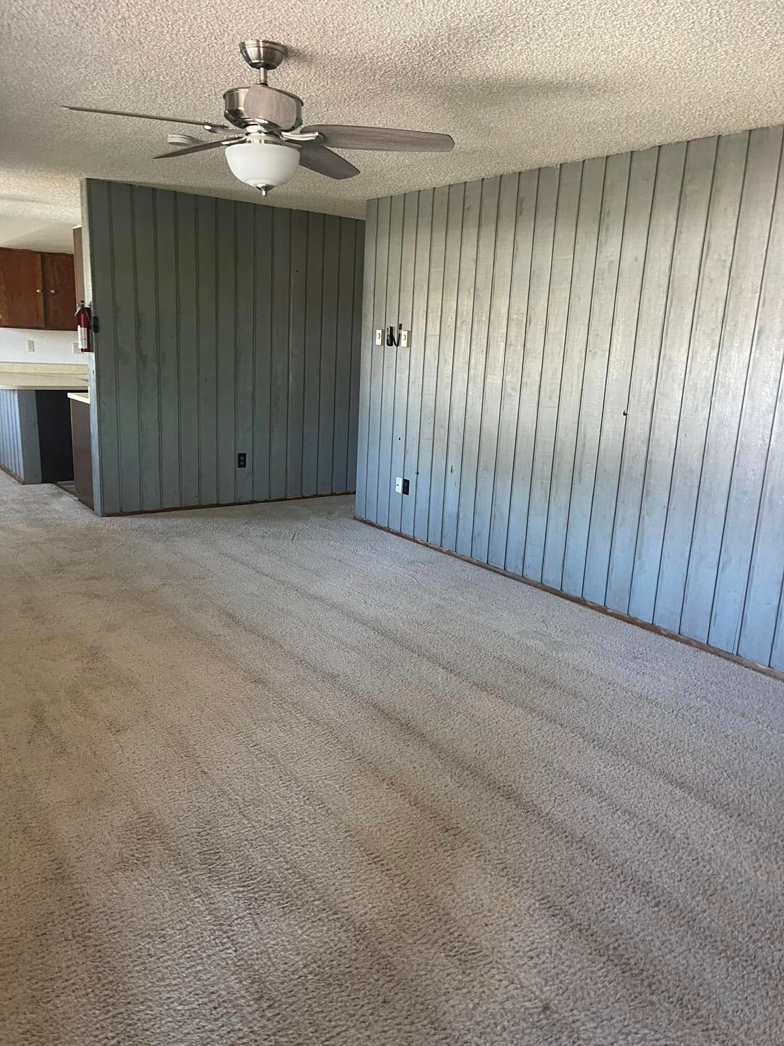 A living room with a ceiling fan and a gray wall.