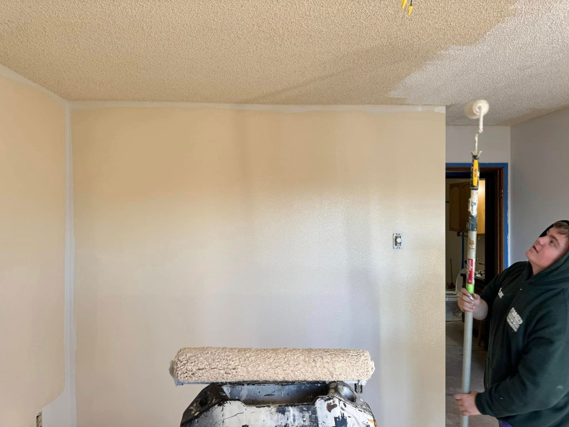 A man is painting the ceiling of a room with a roller.