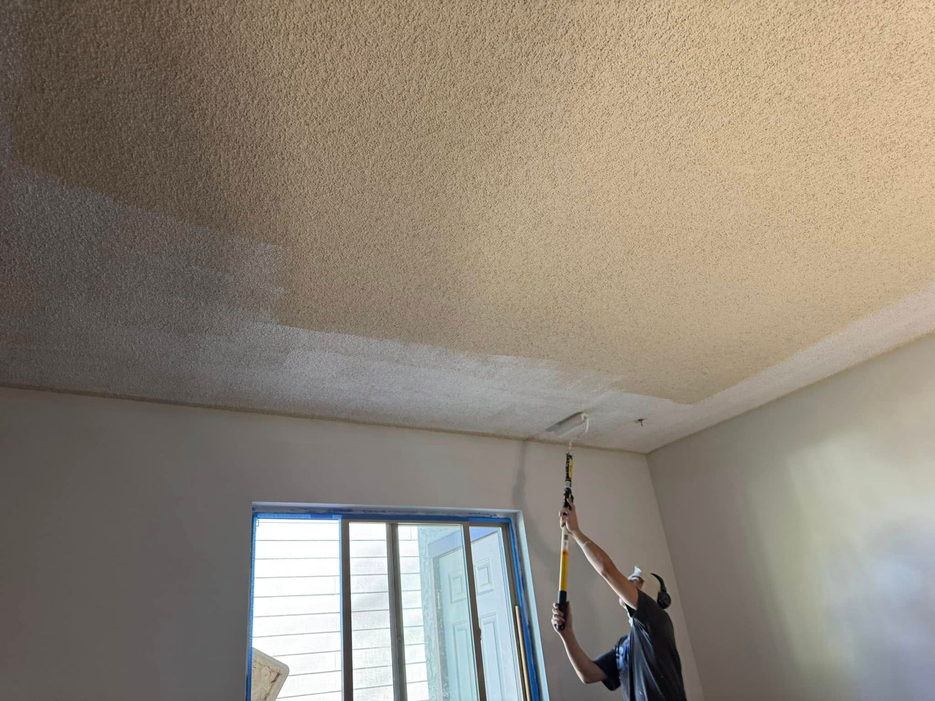 A man is painting the ceiling of a room with a hammer.