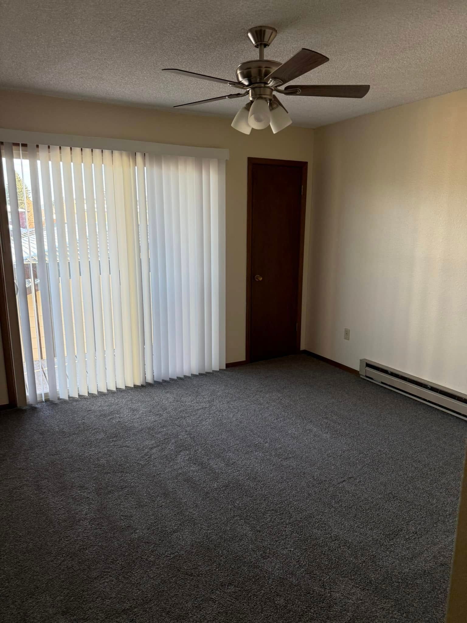 An empty living room with a ceiling fan and sliding glass doors.