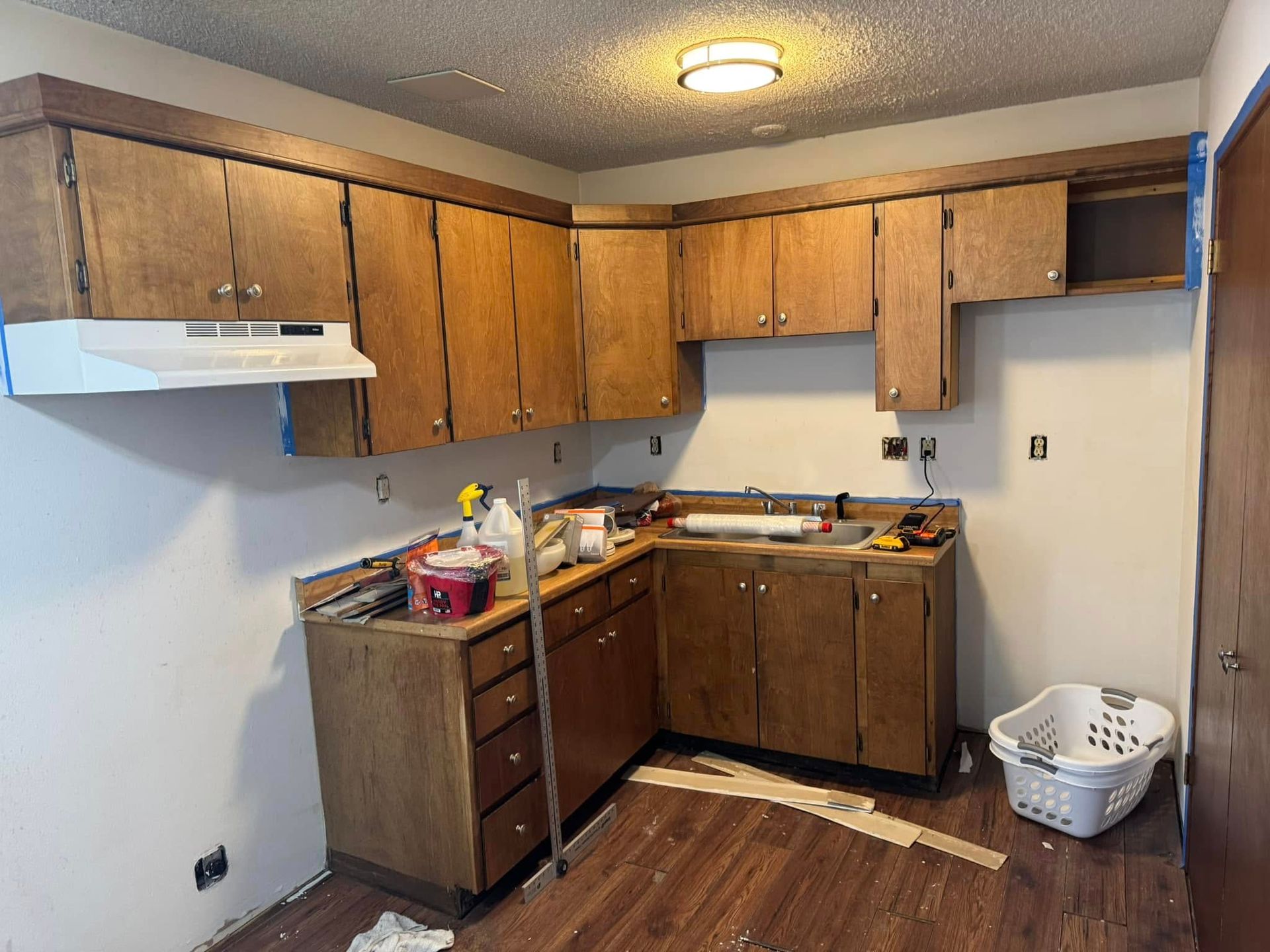 A kitchen with wooden cabinets and a white basket on the floor.