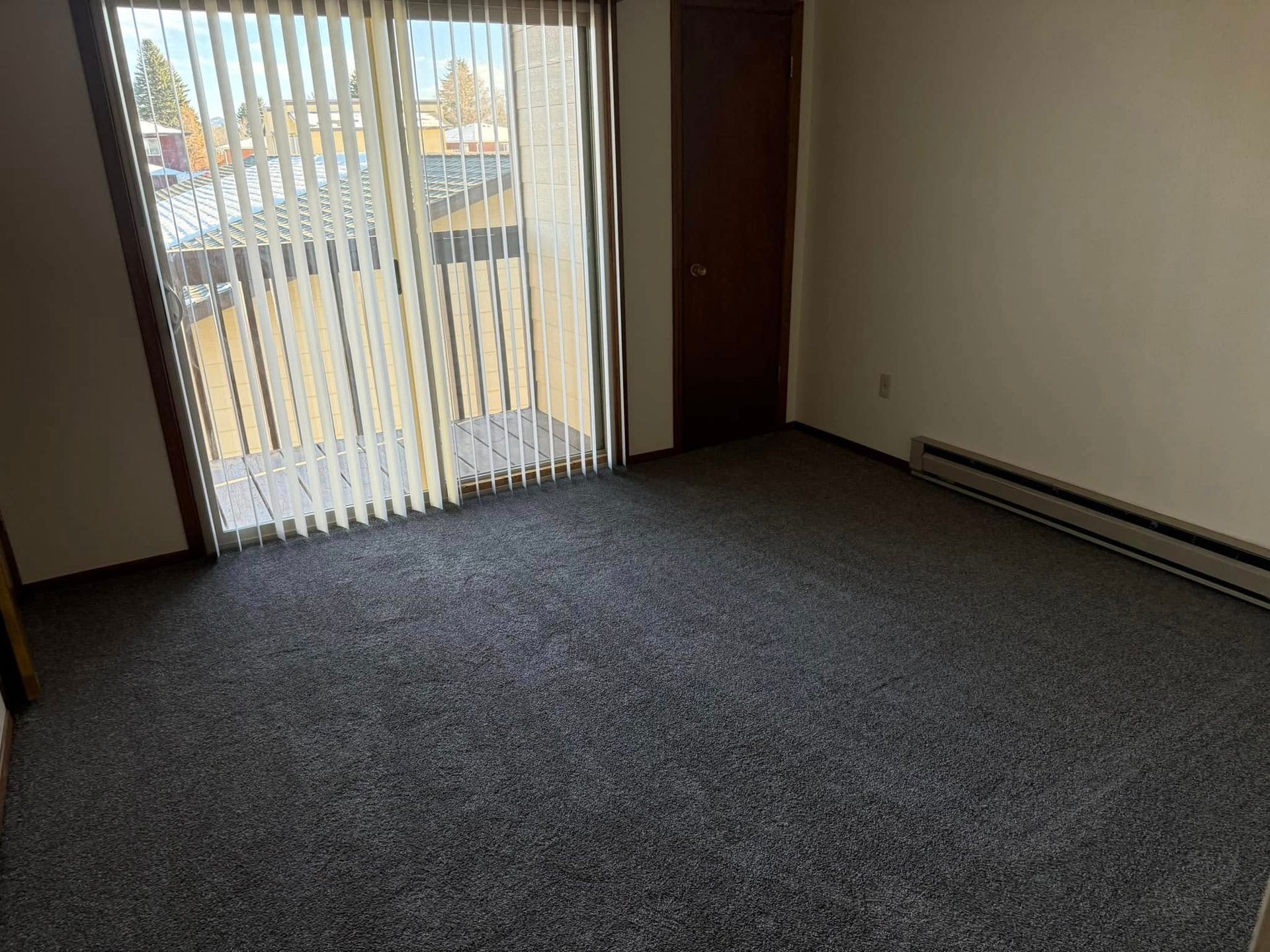 An empty living room with a sliding glass door and blinds.