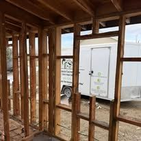 A white trailer is parked in the backyard of a house under construction.
