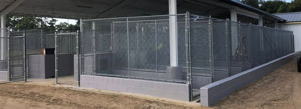Chain-link fence in foreground; warehouse loading docks and trucks blurred in background. Chain-link fence in foreground; warehouse loading docks and trucks blurred in background.