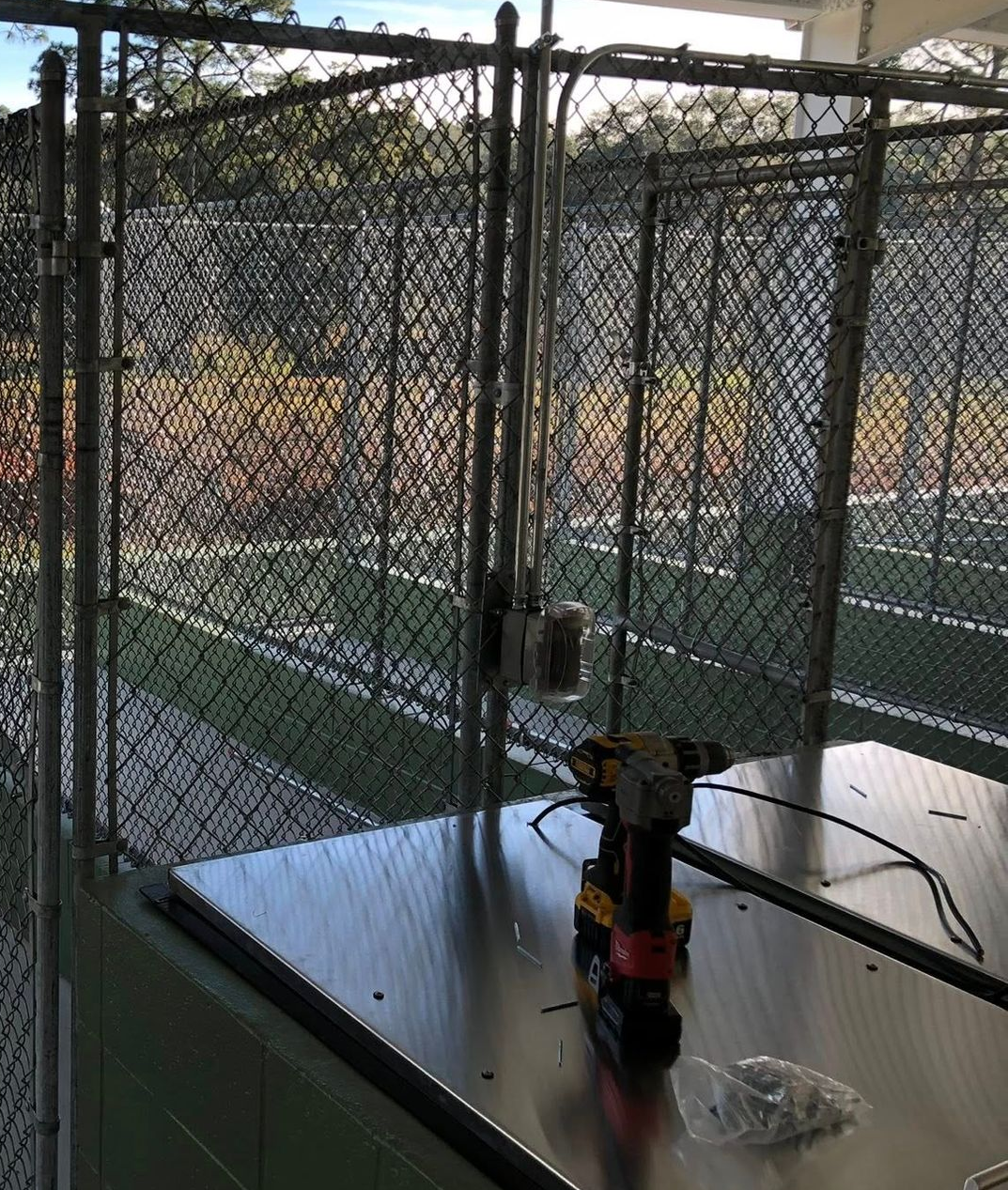 Person using a drill to secure a brown metal fence panel to a horizontal metal beam outdoors. Person using a drill to secure a brown metal fence panel to a horizontal metal beam outdoors.