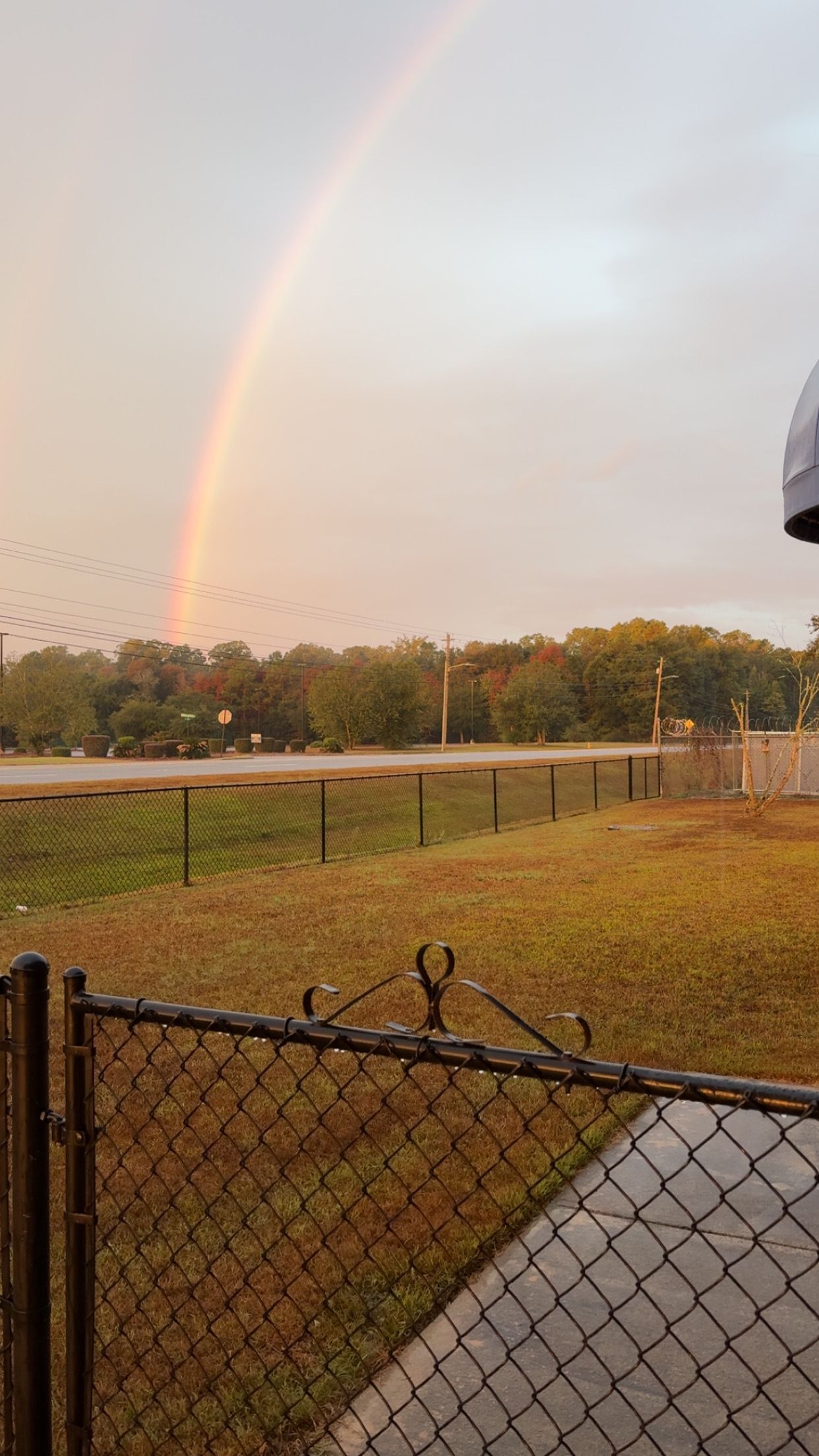 Person using a drill to secure a brown metal fence panel to a horizontal metal beam outdoors.