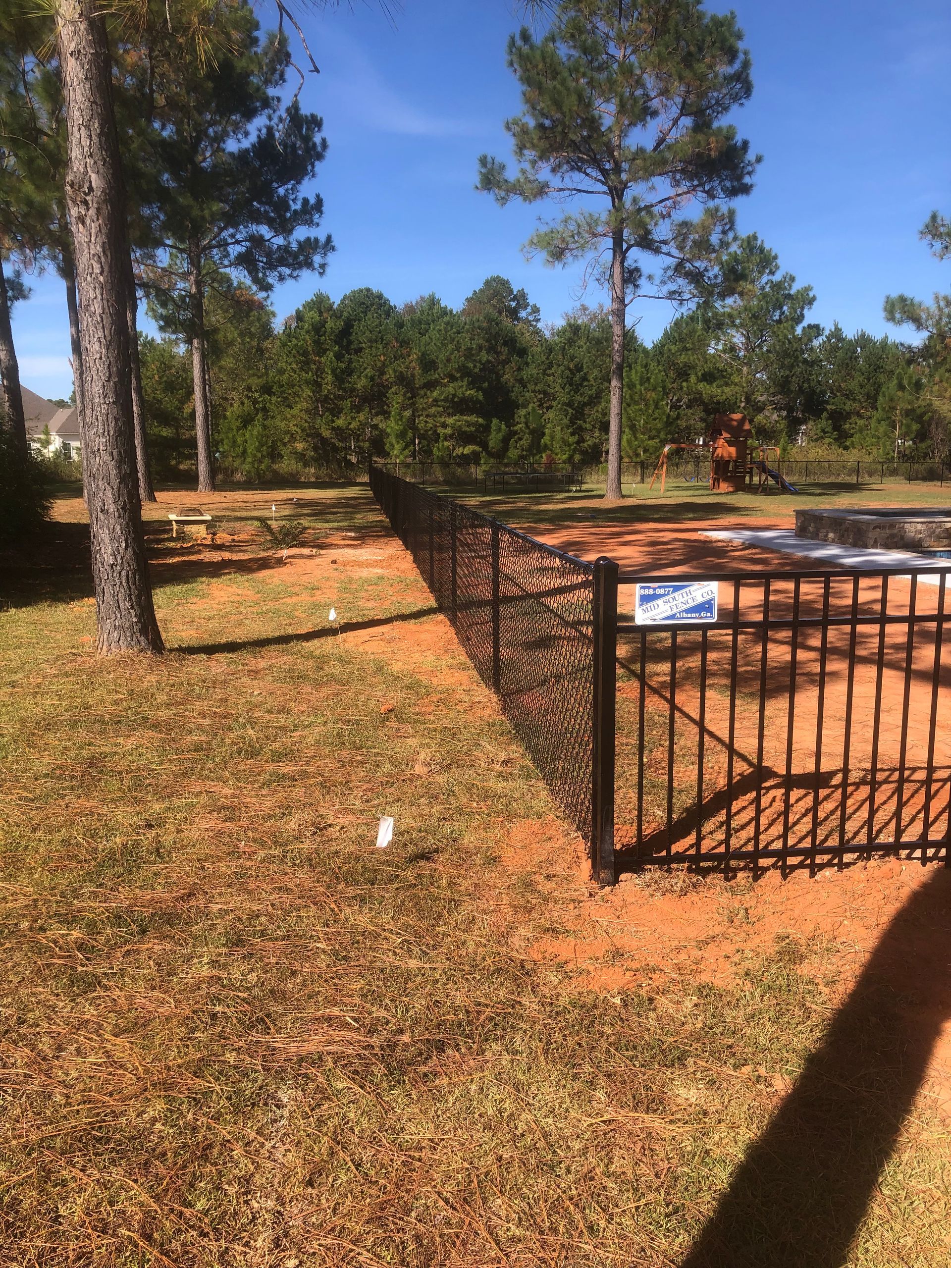 Chain-link fence in foreground; brick building with windows in background, pathway.