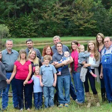 Large family portrait outdoors by water; mix of adults and children, smiling.