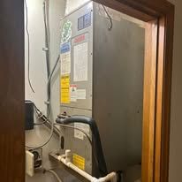 HVAC unit in a utility closet, with visible pipes and wires.