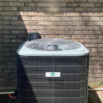 An air conditioning unit, in front of a brick wall, with a fan on top.