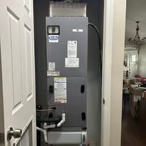 HVAC unit in a utility room; metal and gray, mounted against the wall, with connected pipes.