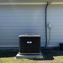 An air conditioning unit sits outside a house with blue siding. Electrical conduit runs along the wall.