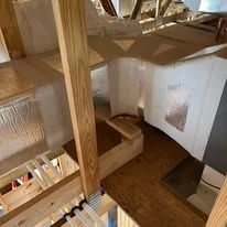 Interior view of a wood-framed attic with insulation and a wooden beam.