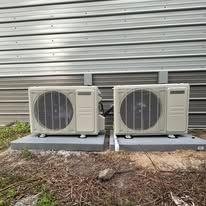 Two beige air conditioning units on concrete pads outside.