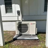 Mitsubishi heat pump unit on concrete near a building's exterior.