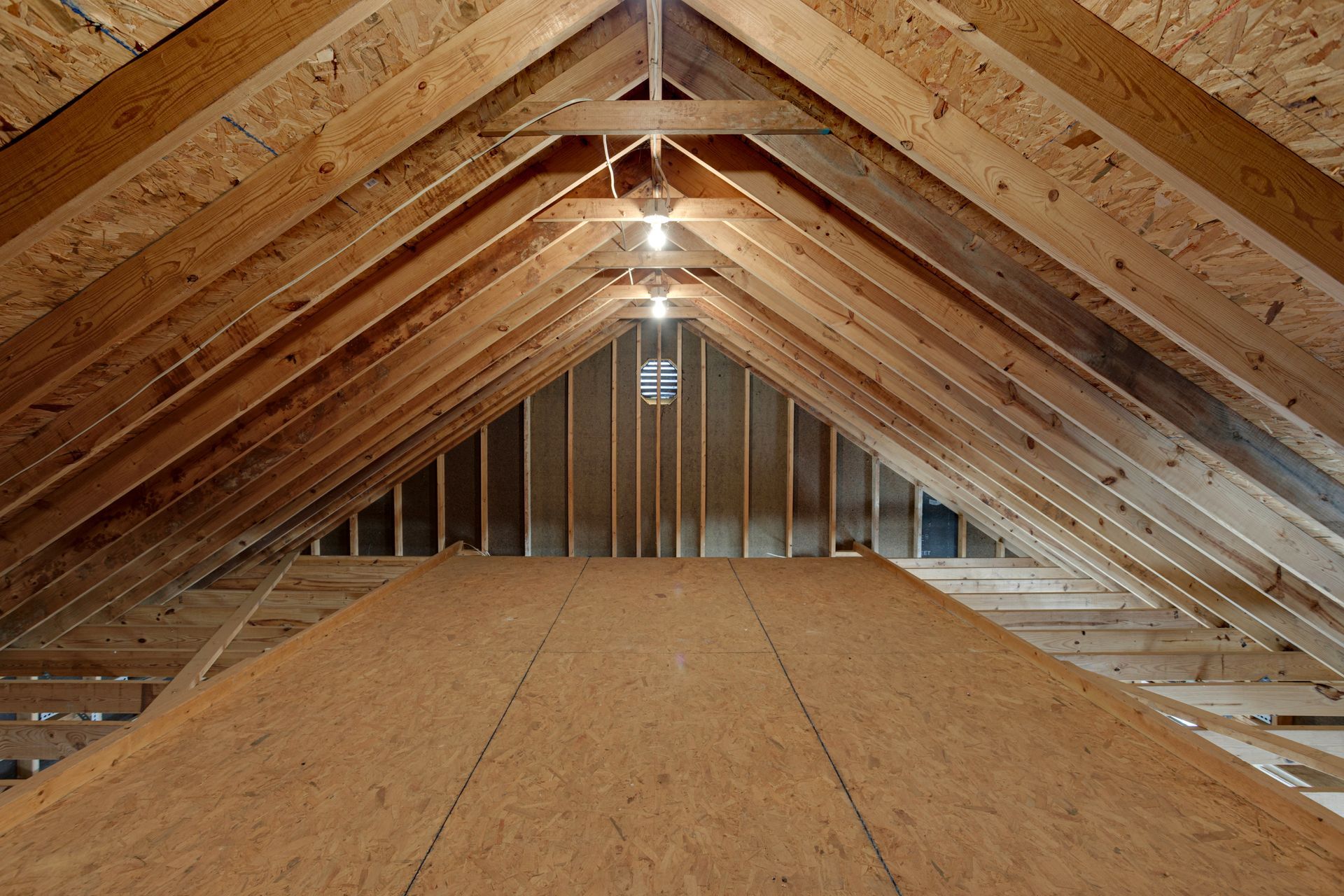 Interior attic view with wooden rafters, a plywood floor, and exposed framing.