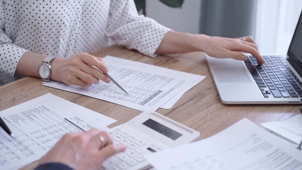 A man and a woman are sitting at a table with papers and a laptop.