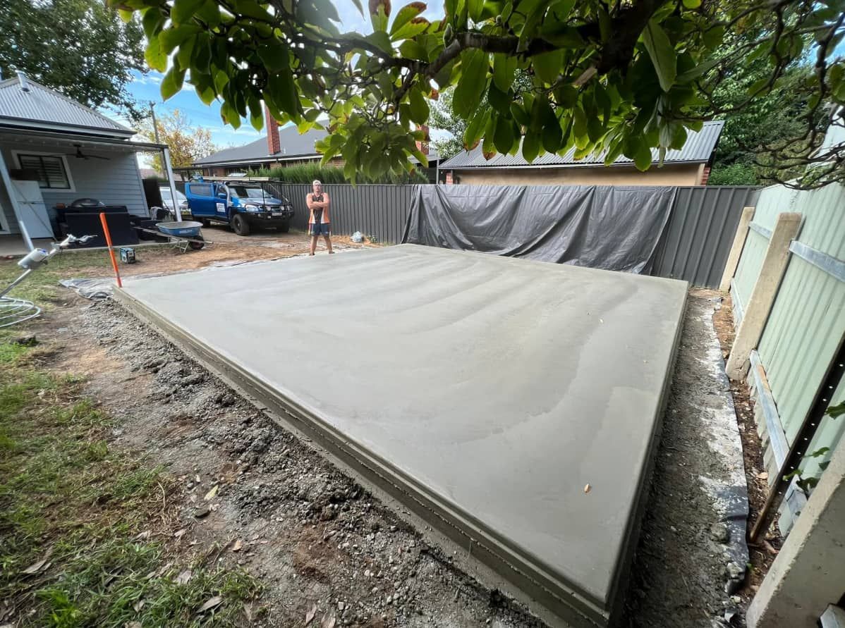 A Man is Standing on a Concrete Slab in Front of a House — Brycey's Concreting In Frederickton, NSW