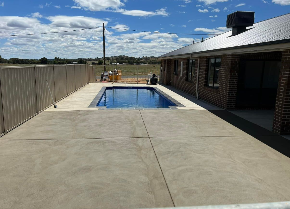 A Large Swimming Pool Beside of Stamped Concreting of a Brick House — Brycey's Concreting In Frederickton, NSW