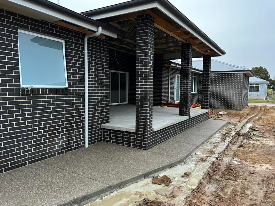 A Brick House With a Porch and a Concrete Walkway — Brycey's Concreting In Frederickton, NSW