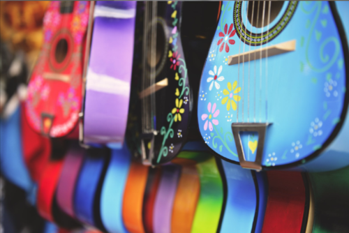 Multiple colored guitars with designs on them hanging on a wall