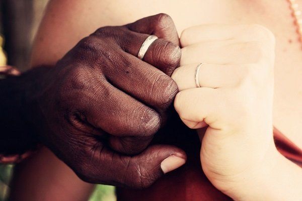 The hand of a black man and a white woman, both showing their wedding rings