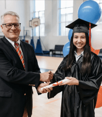 A white man in a suit & tie shaking the hand of an Asian woman who is graduating