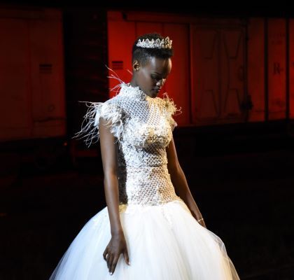 A young black woman looking down, wearing a white wedding dress, with a crown on her head