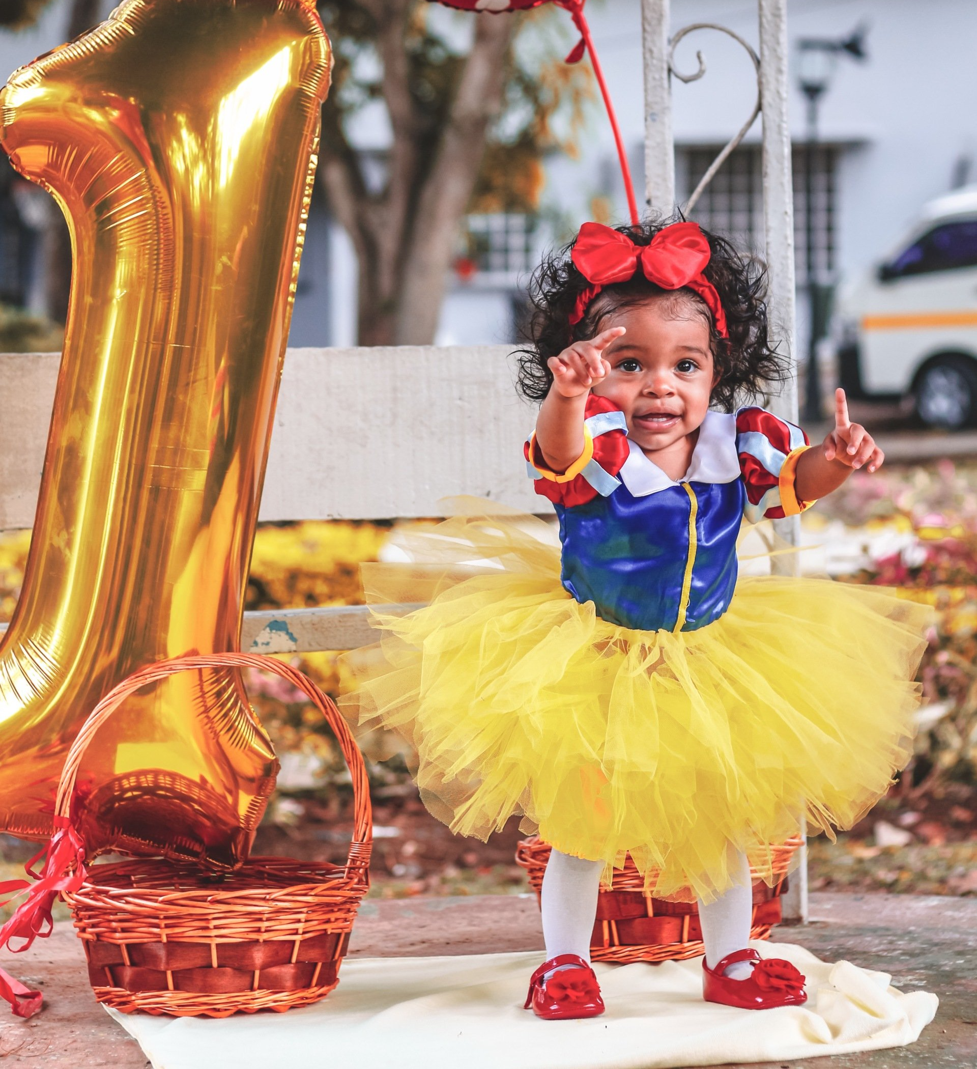 A Black toddler in a Minnie Mouse outfit with a large gold number 1 next to her