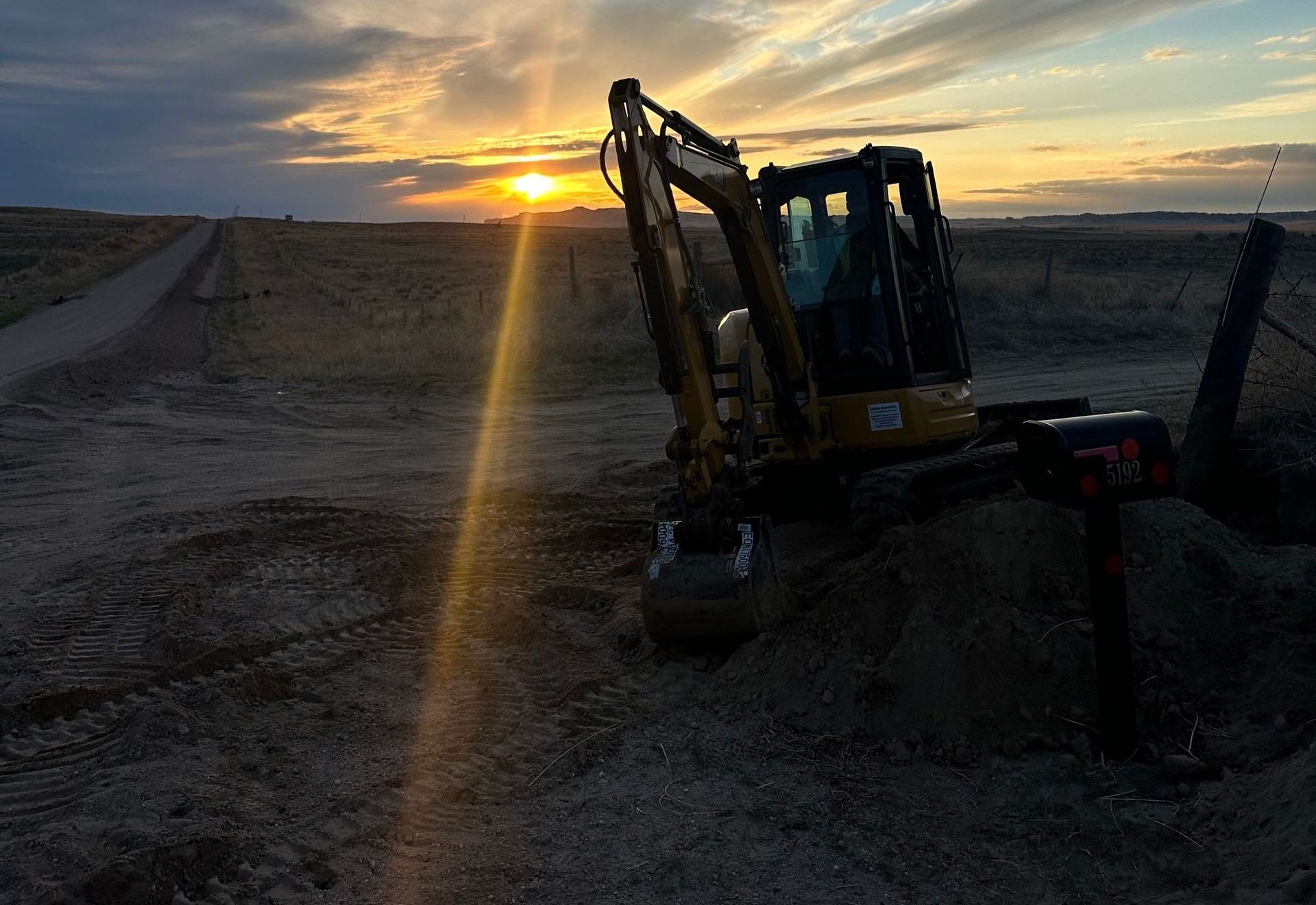 An excavator is sitting in the middle of a dirt field at sunset.