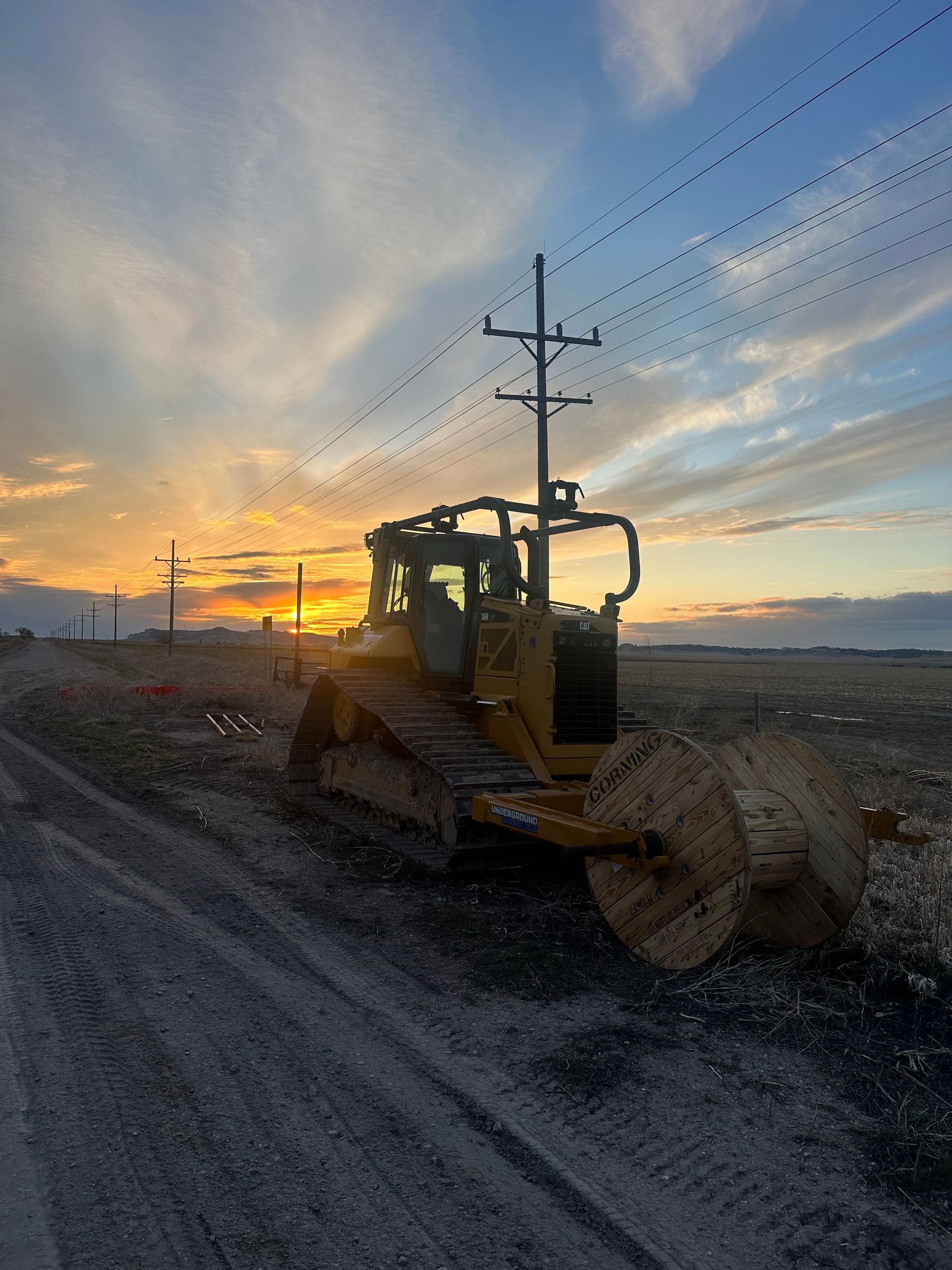 A bulldozer is driving down a dirt road at sunset.