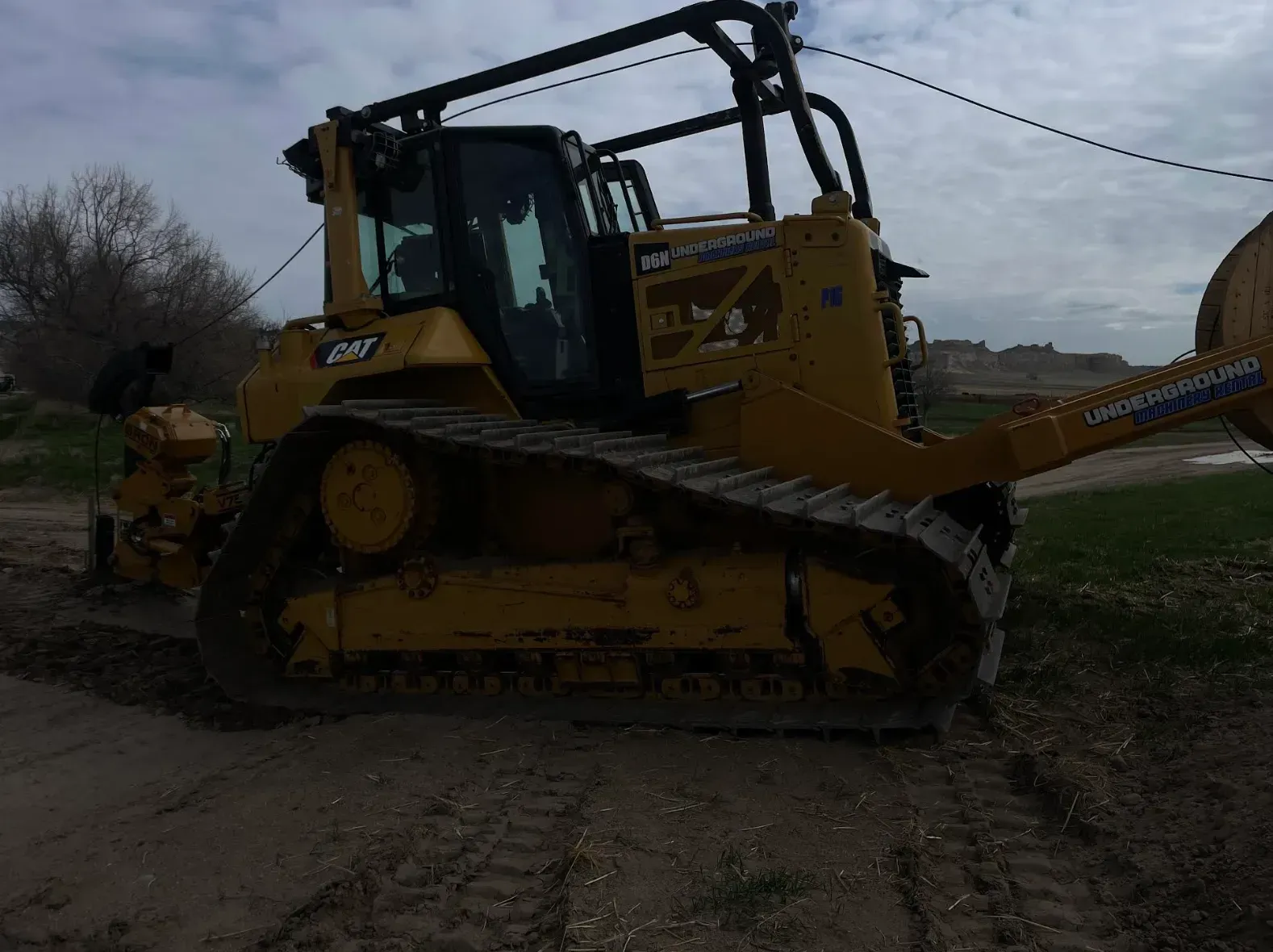 Yellow Caterpillar D8T bulldozer on a dirt road, with roll-over protection and cable reel attached.