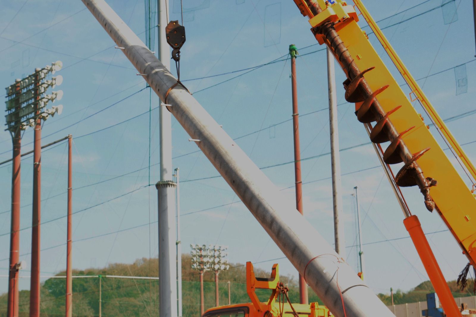 A yellow crane is lifting a pole in a field.