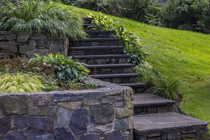 Stone steps ascend a grassy hillside, bordered by stone walls and greenery.
