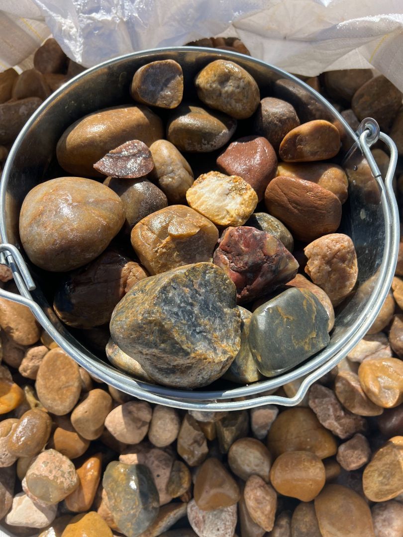 A metal bucket filled with rocks is sitting on top of a pile of rocks.