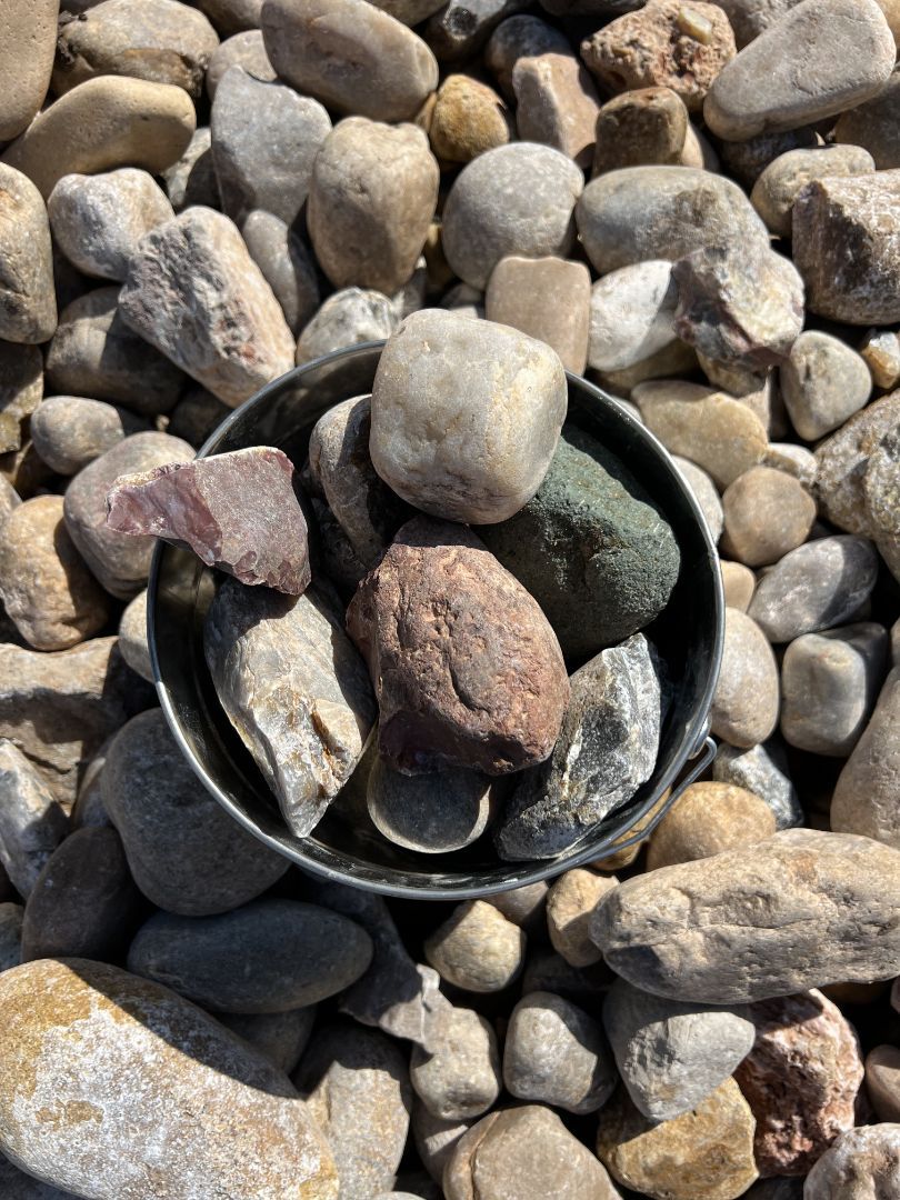 Rainbow river rock in bucket on pile of rock