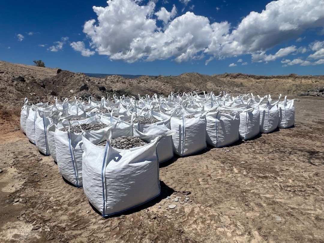 A row of white bags sitting on top of a dirt field.
