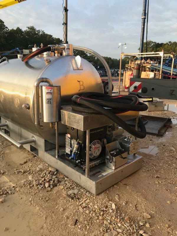 A stainless steel tank with a hose attached to it is sitting on the ground.