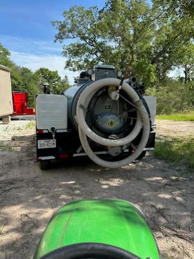 A green tractor is driving down a dirt road next to a vacuum truck.