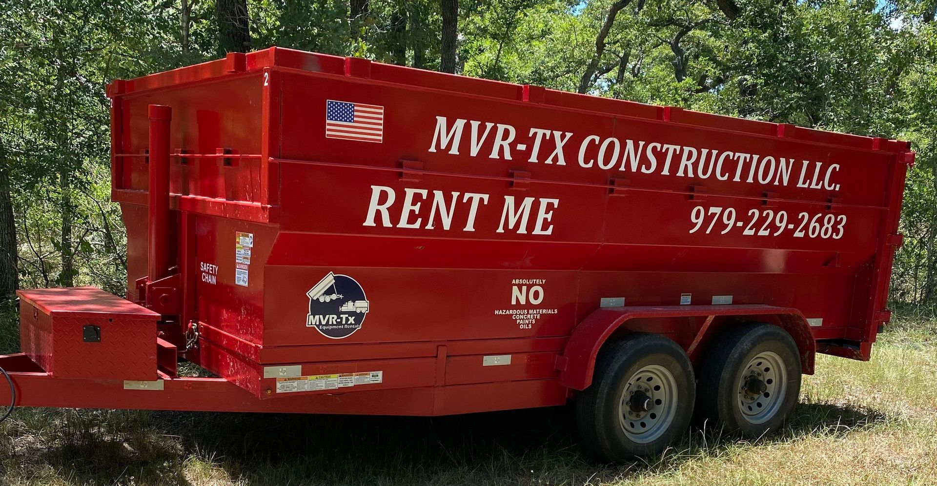 A red dumpster trailer for mvr-tx construction llc is parked in a field.